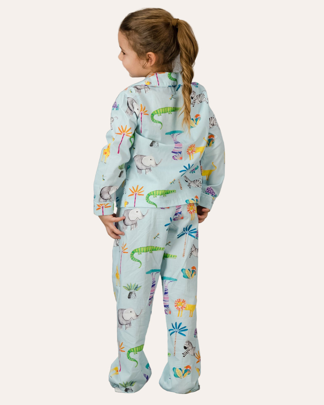 A rear view of a child wearing a long pyjama set with blue dinosaur print on a grey background