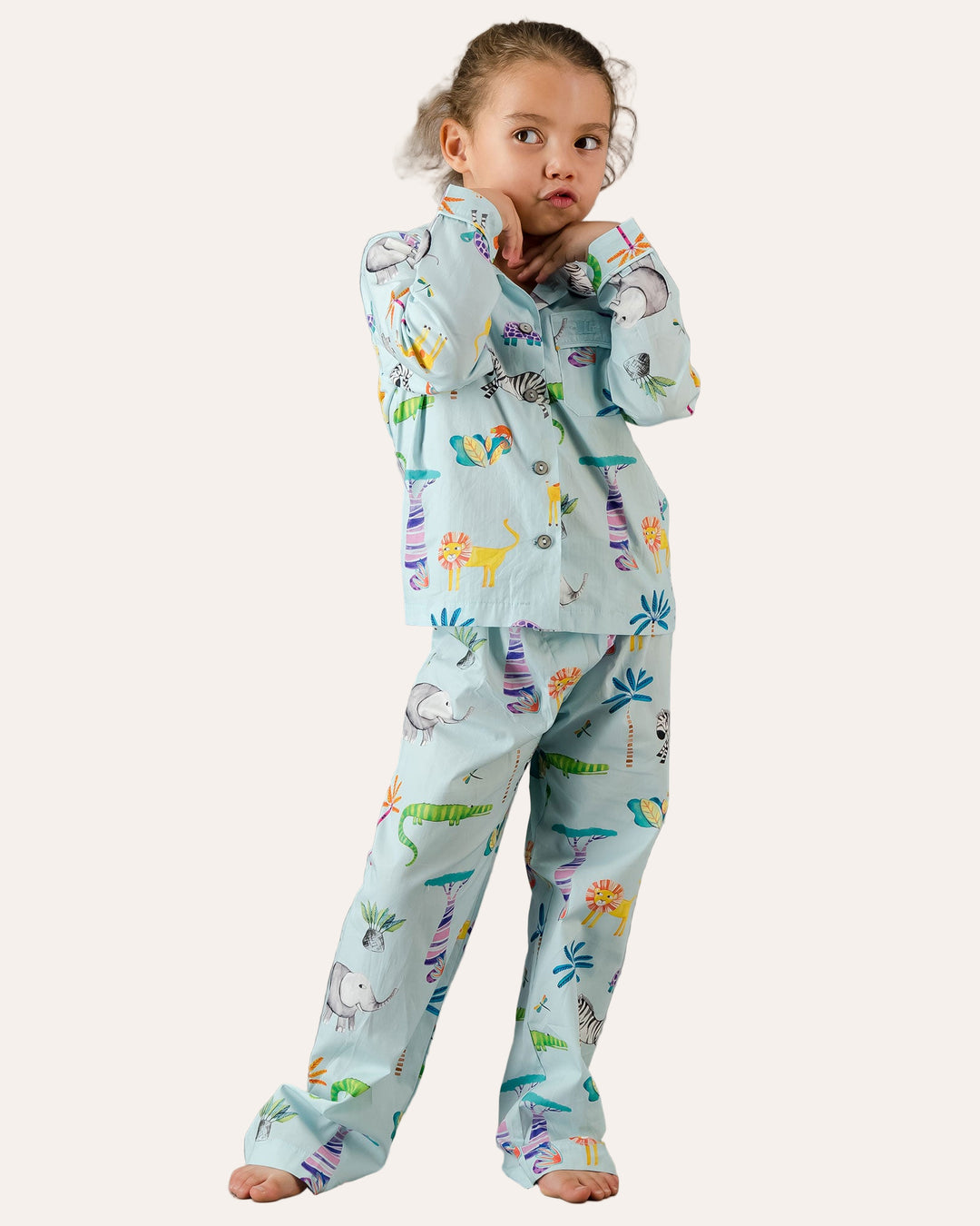 Child wearing a long pyjama set with blue dinosaur print on a grey background