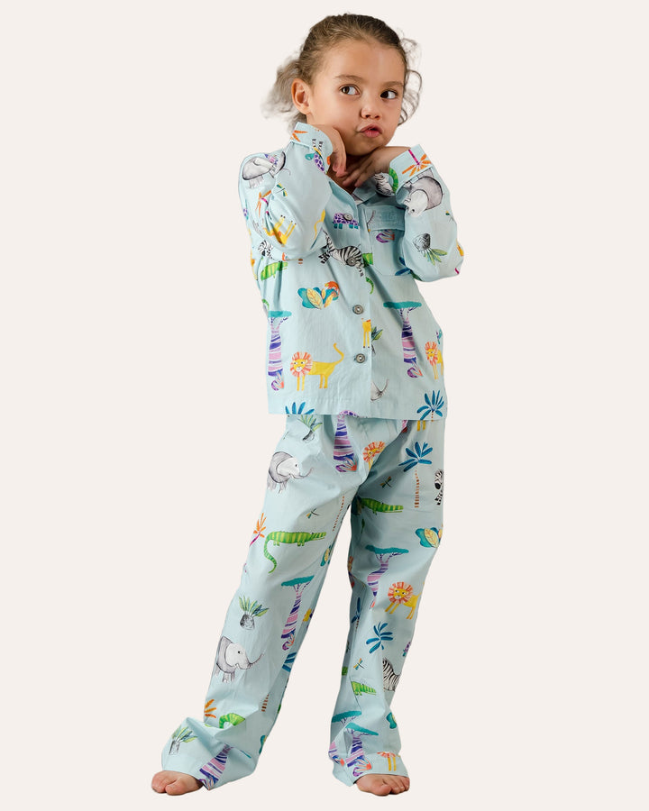 Child wearing a long pyjama set with blue dinosaur print on a grey background