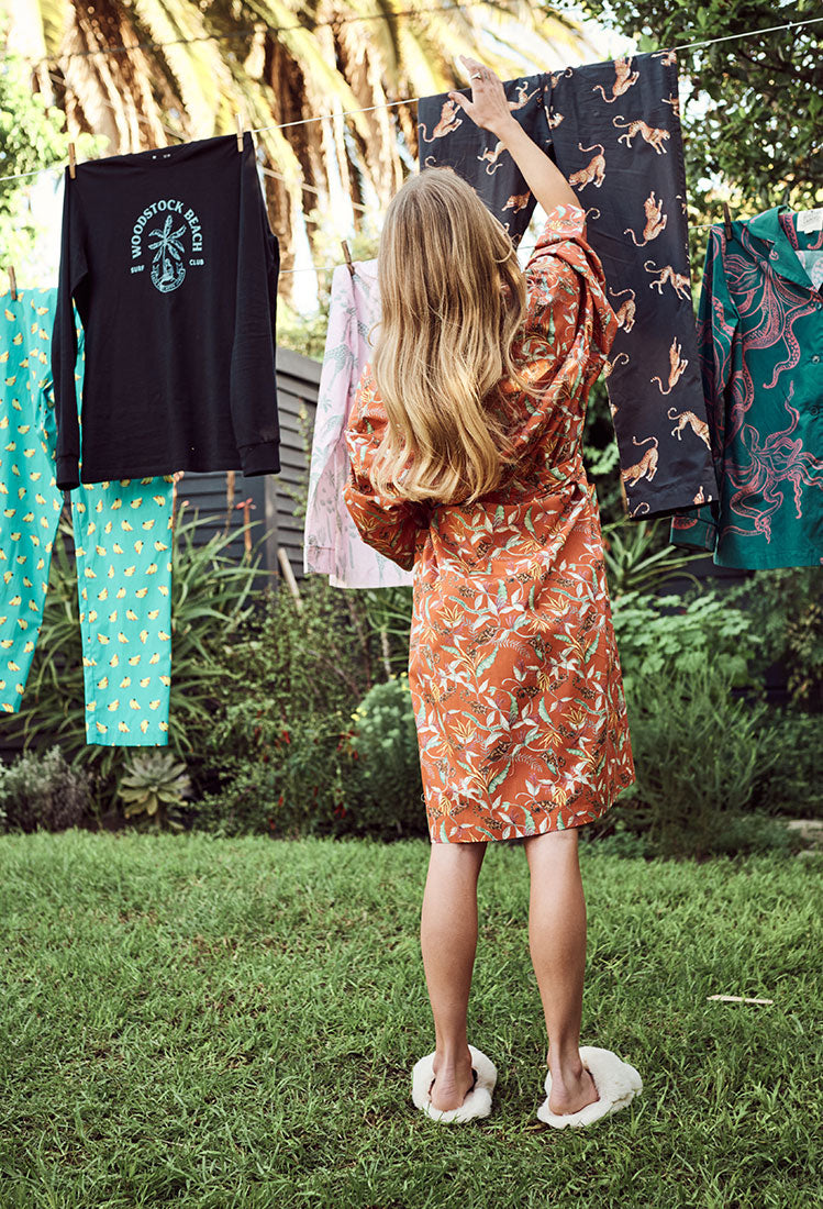 Woman wearing a dressing gown hangs up sleepwear on a washing line.