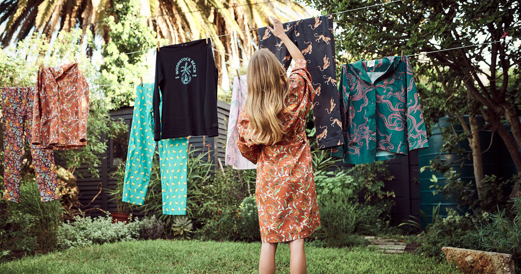 Woman wearing a dressing gown hangs up sleepwear on a washing line.