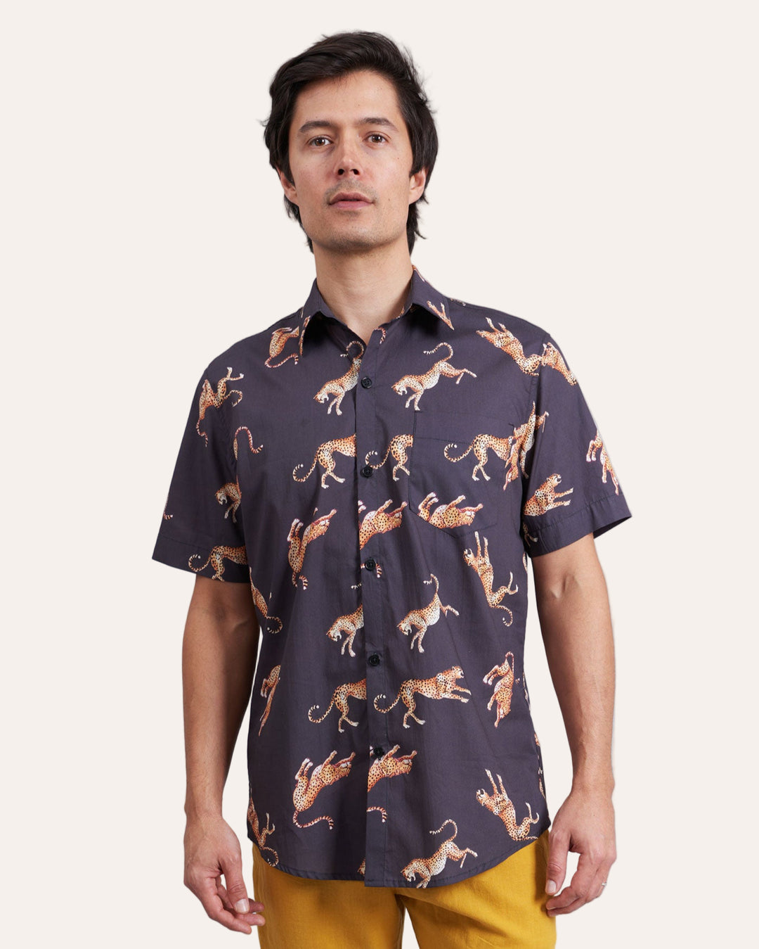 Man wearing a patterned shirt with Jumping Cheetahs designs and yellow shorts on a plain background
