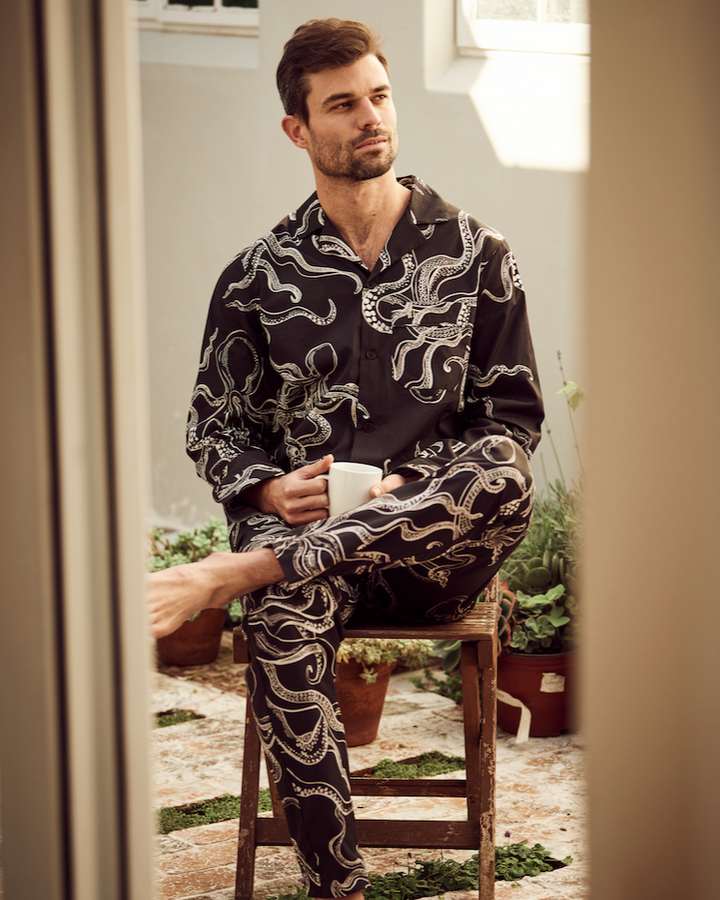 Model enjoying a cup of coffee in men’s black octopus organic cotton long pyjamas