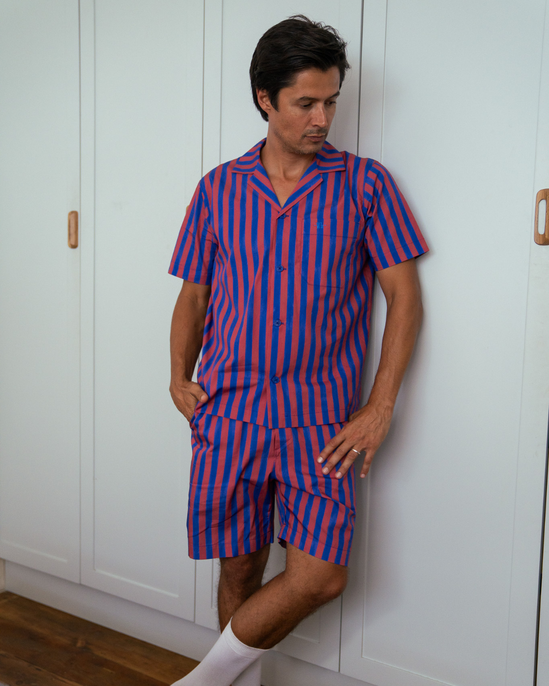 Man leaning against a cupboard wearing a short red and blue striped pajama set 