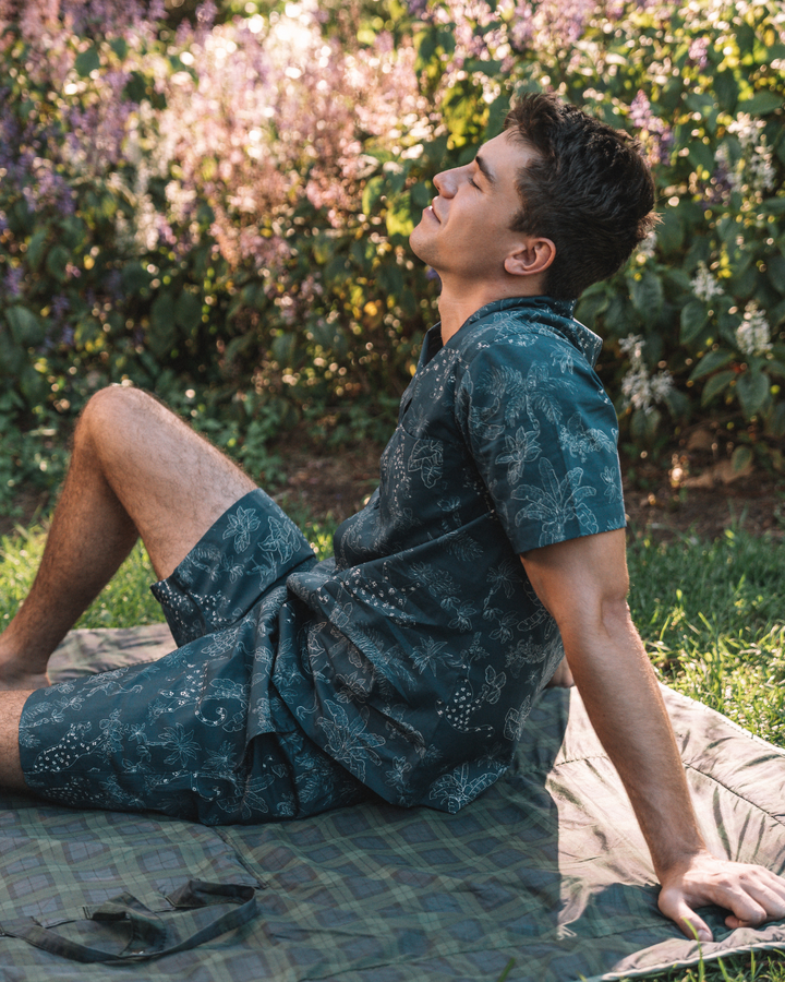Man lounging on a picnic blanket wearing a navy organic cotton short pyjama set in a tropical leopard print