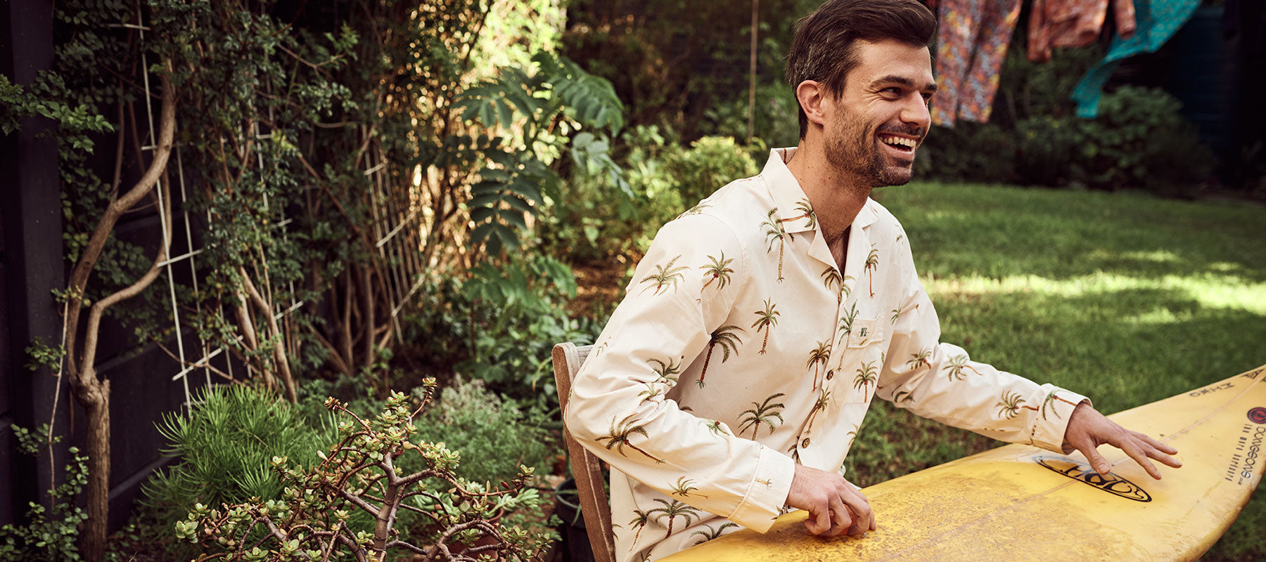 Man waxing his surfboard, wearing Palm Beach Long Pyjamas from Woodstock Laundry